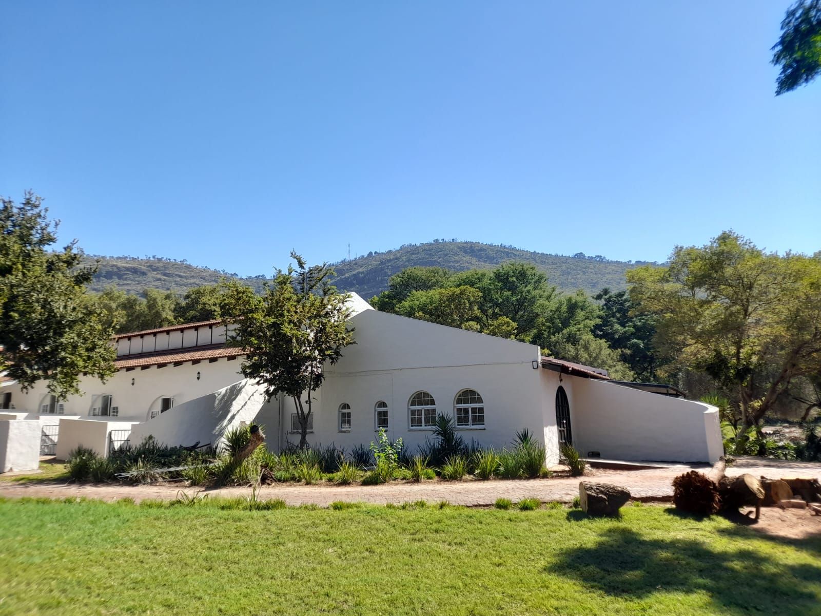 The white Cape-style buildings of Aloe Valley Wellness Manor on a green lawn, with the Magaliesberg mountains behind